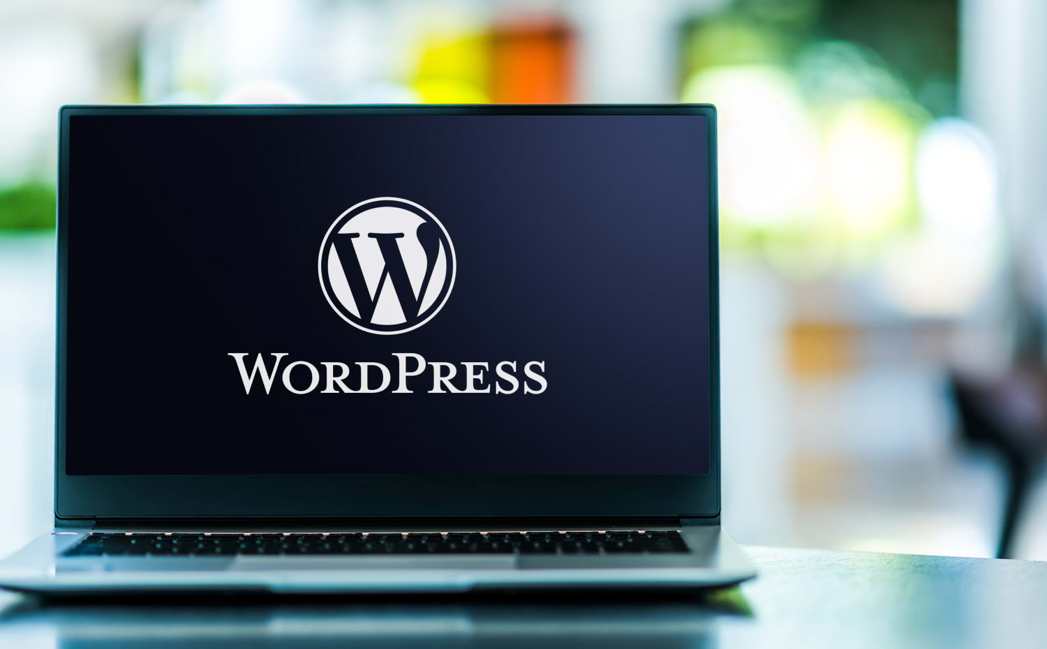 An open laptop sits on a desk. The WordPress logo is on the screen.